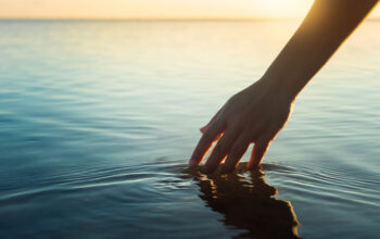A woman feeling and touching the ocean water during sunset